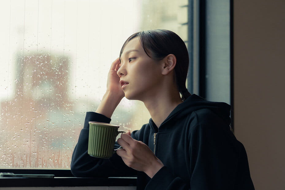 カフェでコーヒーを飲みながら、雨の風景を見る女性