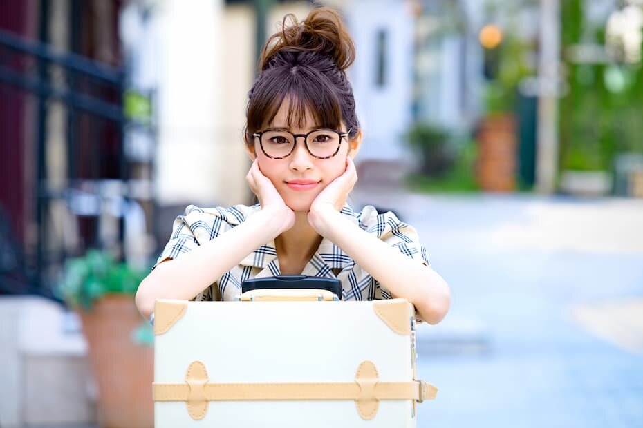 旅行鞄に寄り掛かりながら休憩する笑顔の女性