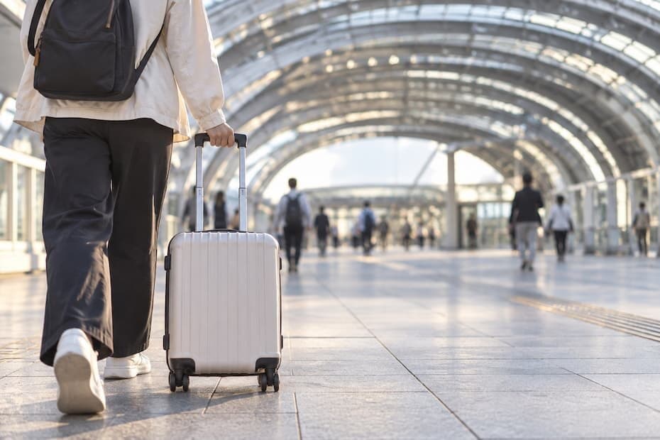 早朝の駅前デッキを、小さめのキャリーケースを引いて歩く旅行者の後ろ姿